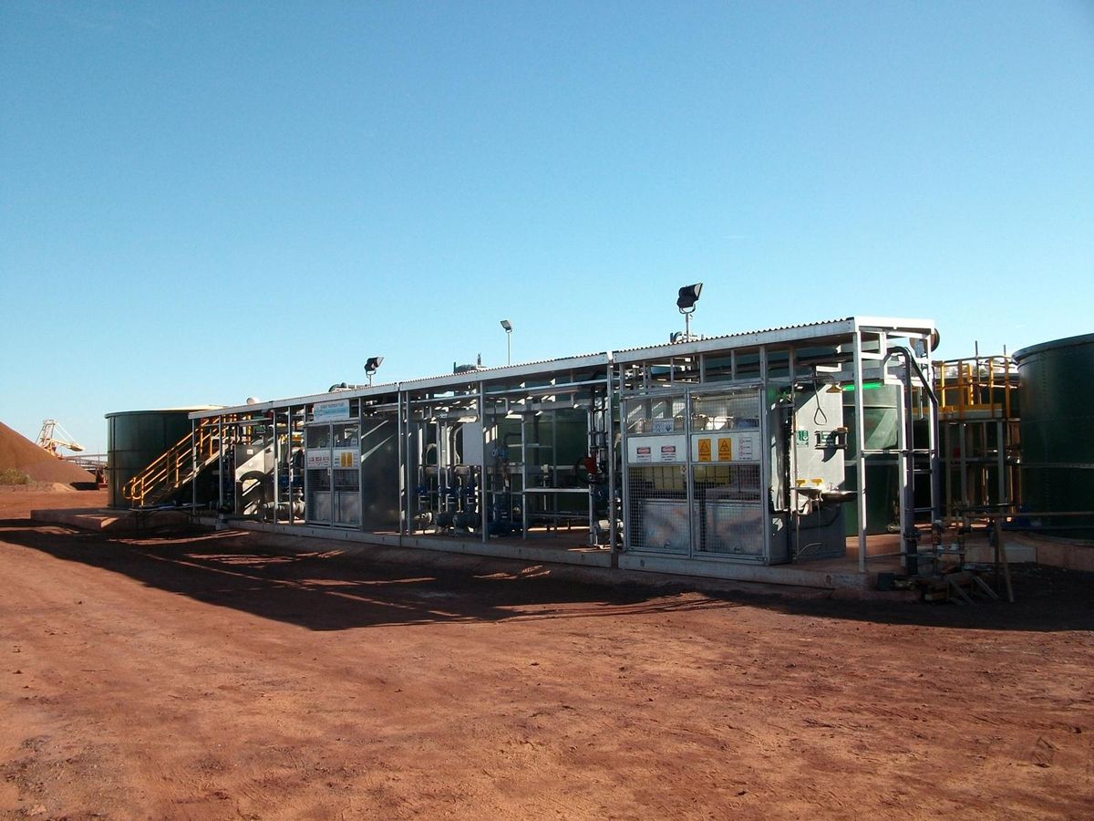 A packaged treatment plant in service at a remote site, its equipment under a roofed walkway on a concrete pad, with an ore stockpile beyond.